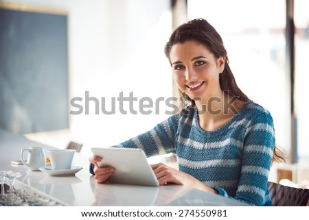 Cheerful woman leaning at the bar counter and using a digital tablet