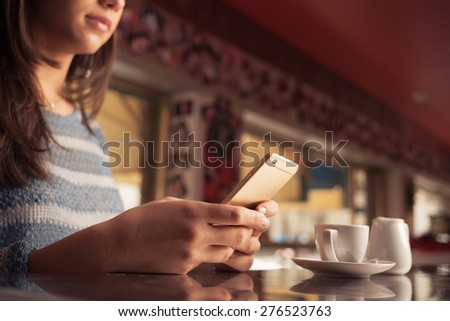 Woman leaning on the bar counter and text messaging with her mobile, hands close up