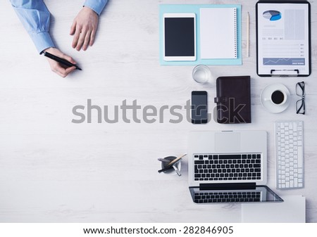 Creative businessman working at office desk and sketching with a black marker, computers and other objects on the right, hands detail top view