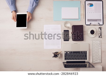 Businessman working at office desk and using a digital touch screen tablet hands detail, computer and objects on the right, top view
