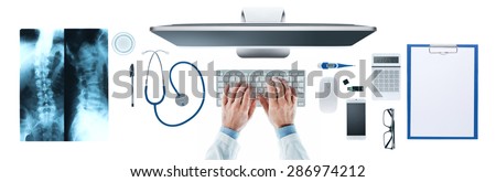 Doctor at desk working at computer with medical equipment on white background, hands close up, top view