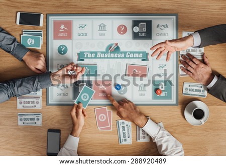 People playing a business board game on a wooden table, rolling dices and holding cards, top view