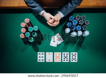 Poker player\'s hands with cards and stacks of chips all around on green table, top view