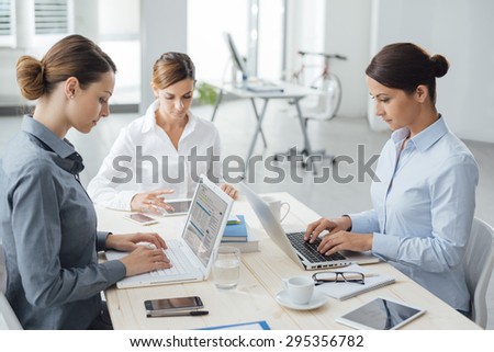 Confident professional women entrepreneurs working at office desk, they are typing on a laptop and using a tablet