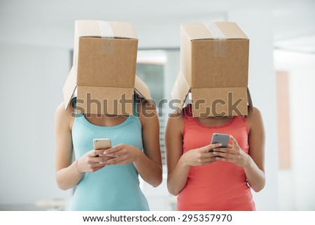 Girls with a box on their heads texting with a smart phone, social isolation and lack of communication concept