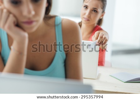 Student girls in the classroom sitting at desk and passing a cheat sheet during a test, selective focus