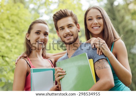 Back to school, group of young students and friends posing at the park, they are holding notebooks and smiling at camera