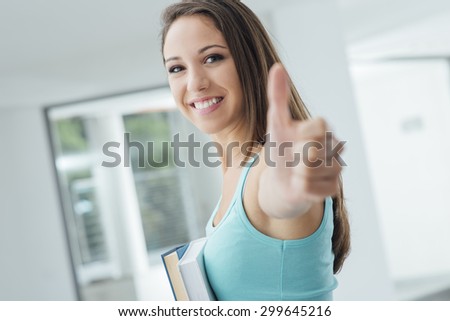 Cheerful student thumbs up and holding books, she has passed the exam, learning and achievement concept