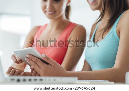 Young female students sitting at desk and using a touch screen tablet
