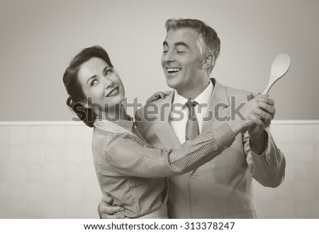 Smiling vintage couple dancing in the kitchen and holding a wooden spoon