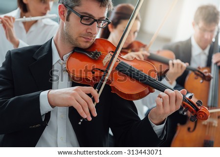 Classical music symphony orchestra string section performing, male violinist playing on foreground, music and teamwork concept