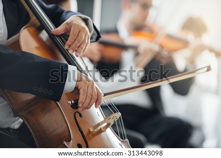 String section of classical music symphony orchestra performing, cellist playing on foreground, hands close up
