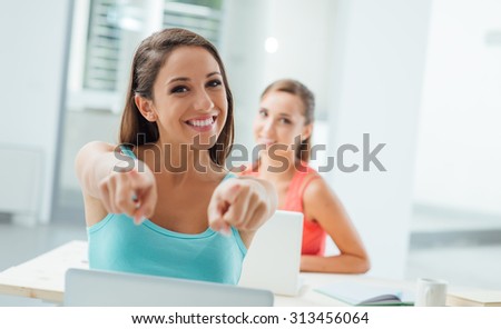 Cheerful student girl pointing at camera and smiling, education and learning concept