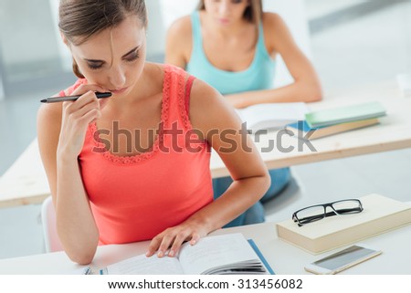 Young female student attending class at school, sitting at desk and reading a book, education and learning concept