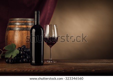Red wine tasting with bottle, wineglass, barrel and grape on the cellar wooden table, red drape on background, still life