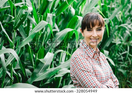 Cheerful female farmer and entrepreneur posing in the corn crop and smiling at camera, agriculture and cultivation concept