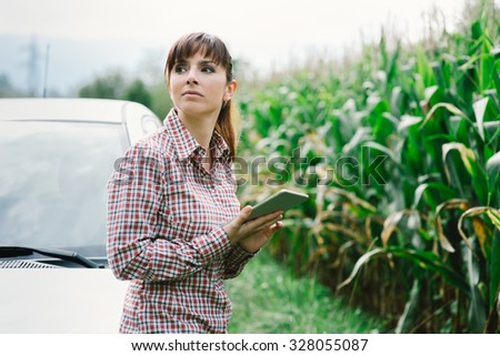 Young sad woman leaning on her car, she got lost in the countryside and she is looking for directions with her digital tablet