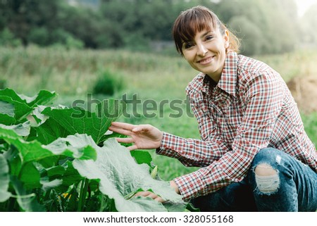 Smiling female gardener posing with zucchini plants and looking at camera, farming and gardening concept