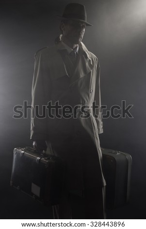 Man in trench coat with hat and luggage leaving in the dark, 1950s style film noir