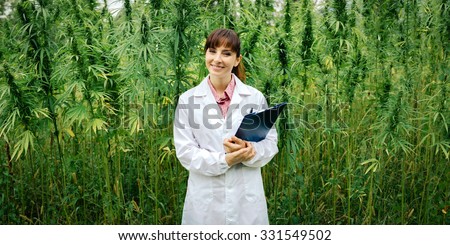 Confident female doctor with clipboard posing in a hemp field, alternative herbal medicine concept