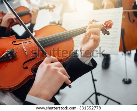 Confident violinist playing his instrument and reading a music sheet, classical music symphony orchestra performing on background