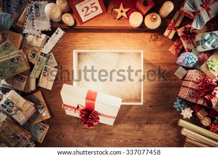 Open empty Christmas gift box on a wooden desktop surrounded by letters and presents, top view