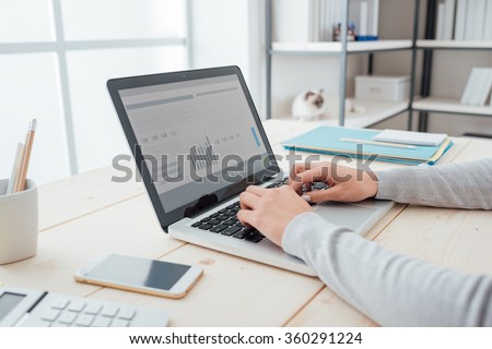 Businesswoman sitting at office desk and typing on a laptop hands close up