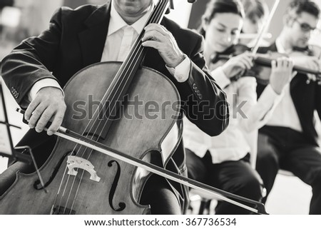 Professional cello player performing with other musicians, classical music symphony orchestra, unrecognizable person