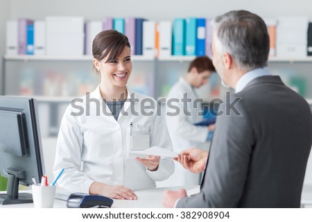 Male customer at the pharmacy, he is giving to the smiling pharmacist a prescription, healthcare concept