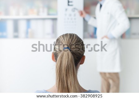 Young woman in the optometrist office examining her eyesight, he is pointing at the chart, eye care concept
