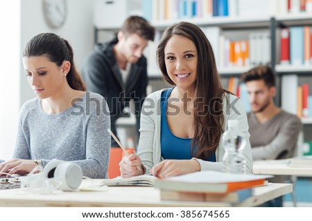 Smiling girls sitting at desk and studying in the classroom, learning and education concept