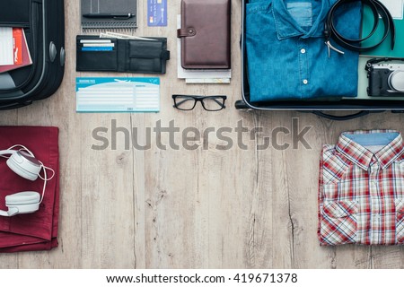 Getting ready for a trip and packing a suitcase before leaving; accessories, clothing and personal items on a desktop, travel and vacations concept