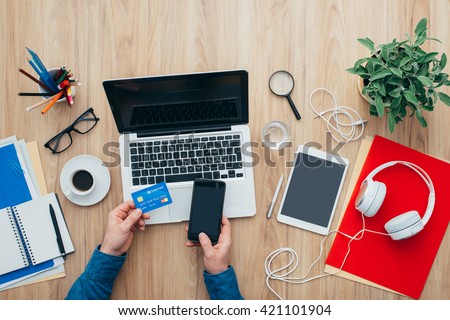 Man shopping online at home using a laptop and a credit card, he is making a mobile payment using his smartphone, top view