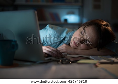 Sleepy exhausted woman working at office desk with her laptop, she is sleeping with eyes closed, working overtime concept