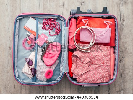 Woman\'s open bag on a desktop with clothing and accessories, she is packing and getting ready to leave, travel and vacations concept
