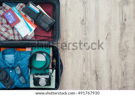 Open traveler\'s bag with clothing, accessories, credit card, tickets and passport, travel and vacations concept, flat lay