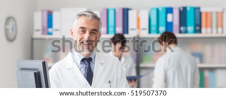 Professional smiling doctor posing at hospital, medical staff working on the background