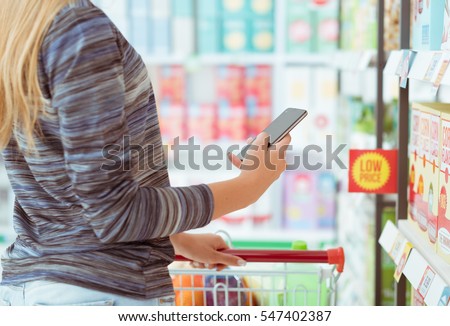 Woman doing grocery shopping at the supermarket, she is searching products and offers using apps on her phone, technology and augmented reality concept