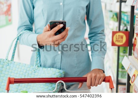 Woman doing grocery shopping at the supermarket, she is searching products and offers using apps on her phone, technology and retail concept