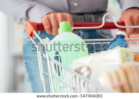 Man doing grocery shopping at the supermarket, he is pushing a full trolley, hands detail close up
