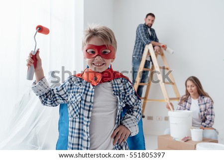 Family renovating their home and painting walls, the boy is wearing a superhero costume and holding a paint roller