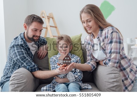 Happy family holding a model house and posing together: home improvement, real estate and mortgage concept