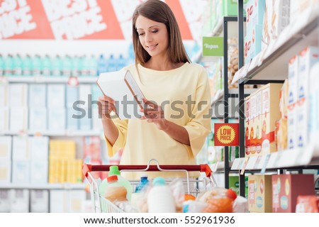 Young woman doing grocery shopping at the supermarket and reading food labels with ingredients on a box, shopping and nutrition concept