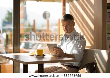 Businessman having a delicious breakfast at the cafe, he is sitting at the table and using a touch screen tablet