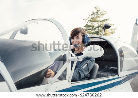 Smiling female pilot in the light aircraft cockpit, she is wearing aviator headset and checking controls