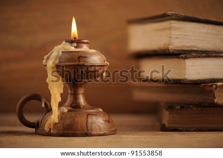 old candle on a wooden table, old books in the background