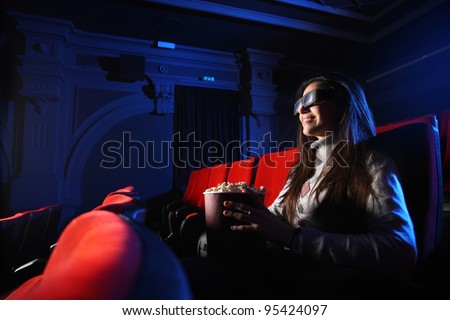 portrait of a beautiful girl with 3D glasses, in a empty movie theater, she eats popcorn and smiles