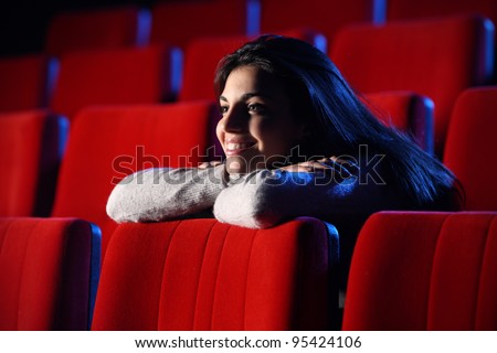 funny movie: portrait of a pretty girl in a movie theater, she leans her elbows on the back row of chairs in front of her, totally relaxed