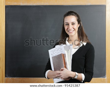 Portrait of a smiling young woman, college student or teacher in front of a blackboard