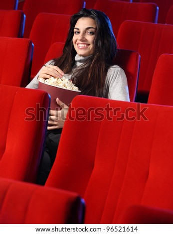 portrait of a pretty young woman, she sitting in an empty theater, eats popcorn and smiles